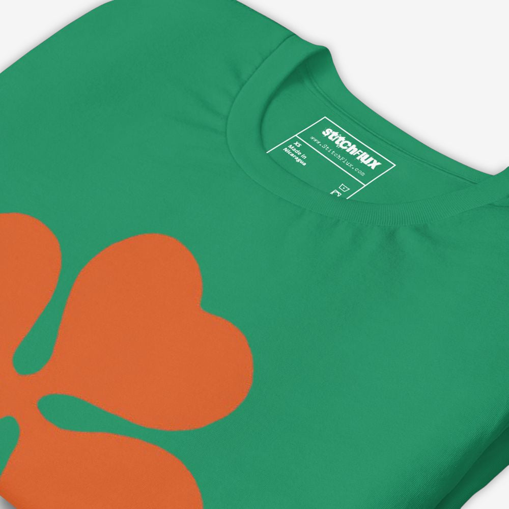 Close-up of the collar of a green T-shirt with an orange clover leaf.