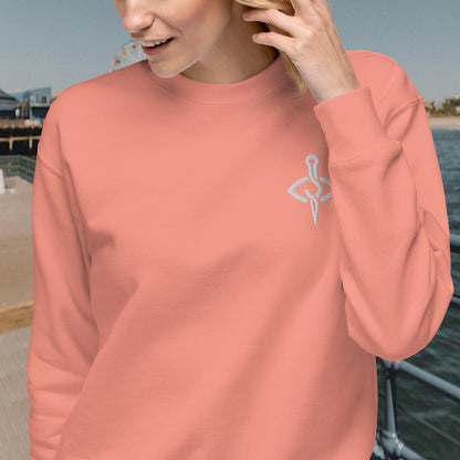 Close-up of a woman wearing a dusty rose sweatshirt featuring a needle and thread design