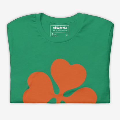 Folded green T-shirt with orange clover design on the front.