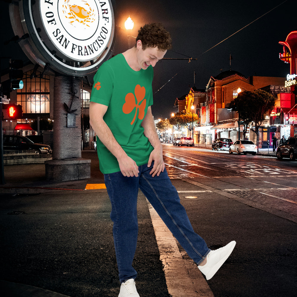 Man wearing a green T-shirt with a clover design, standing on a city street at night.