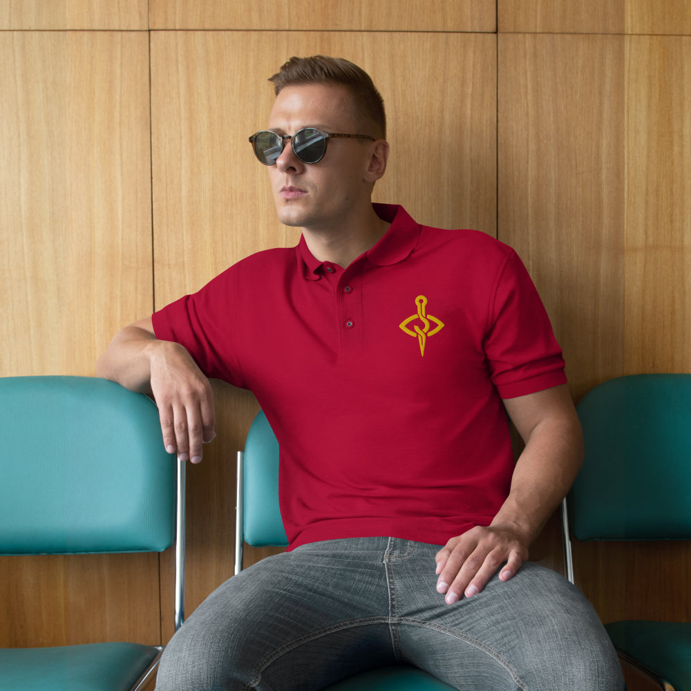 Model wearing a Stitch Art Embroidered Polo in silver with a distinctive needle and thread logo, showcasing a blend of style and craftsmanship. Seated front view. color red.