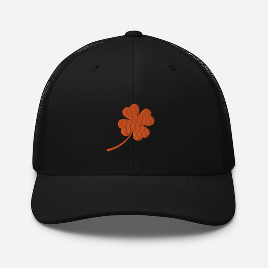 Black trucker hat with a vibrant orange four-leaf clover embroidered on the front, mesh back for increased air flow front view.