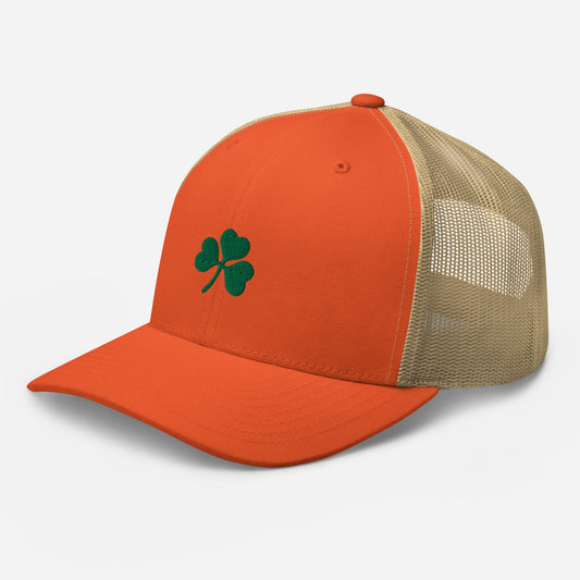 Orange and khaki trucker hat with a 4-leaf clover embroidered on the front panel, showcasing a mesh back for breathability front left view.